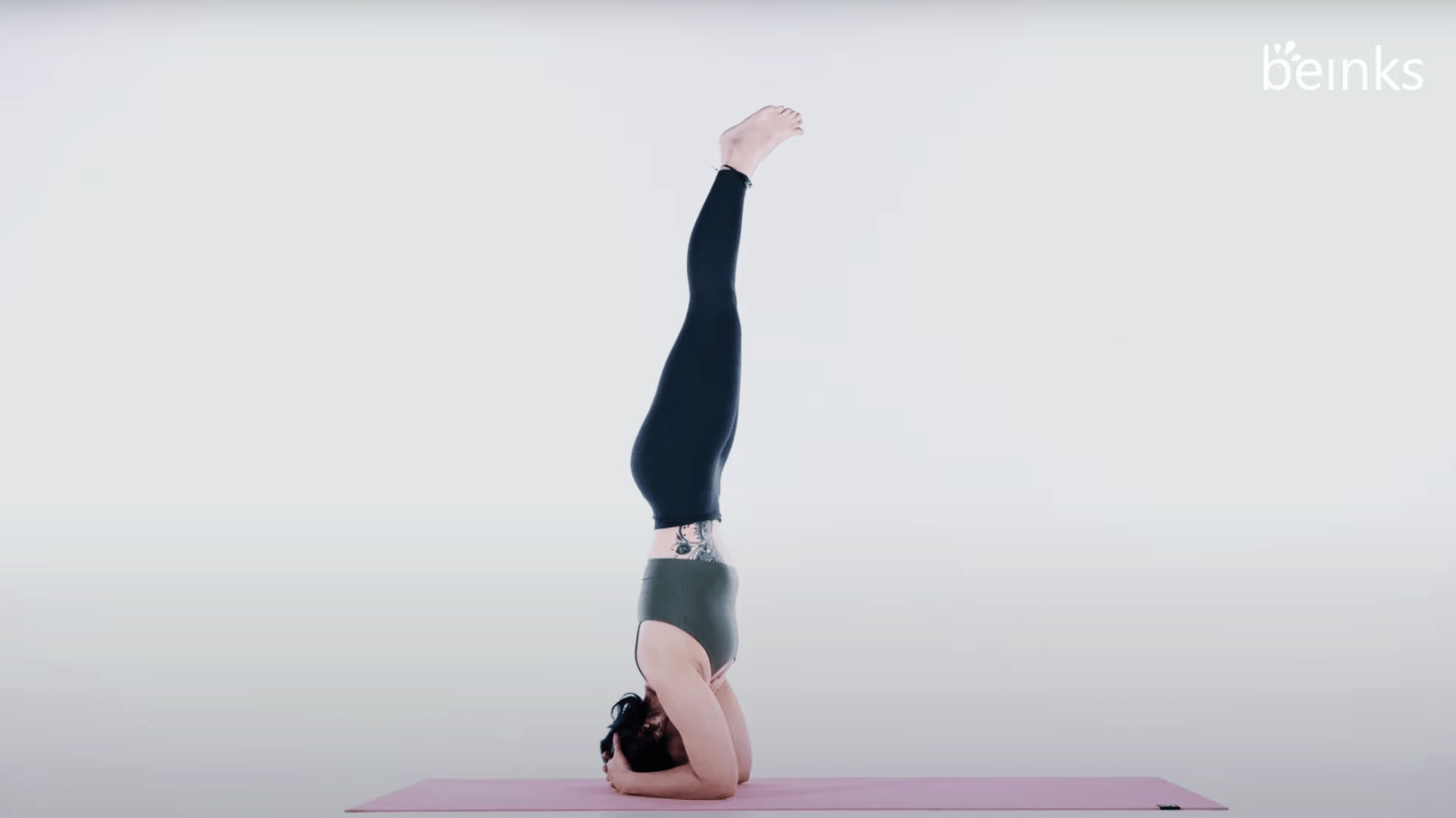 Man doing a sirsasana variation yoga headstand in a gym to align
